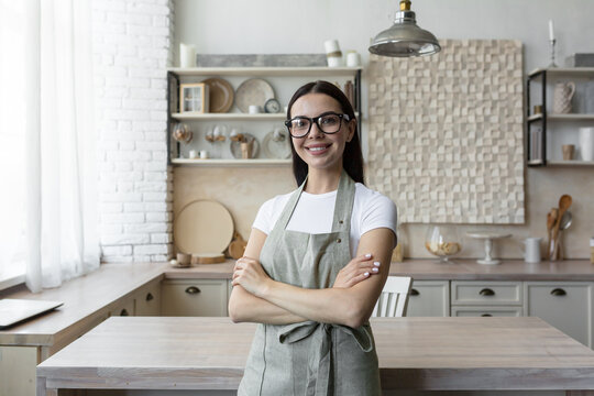 Portrait of a young blogger woman standing at home in the kitchen in an apron and looking at the camera. Blogs about home economics and cooking.