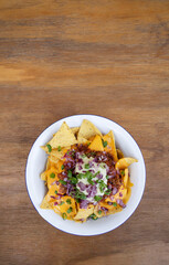 Nachos with chili. Closeup view of nachos with cheddar cheese, avocado cream, red onion pickles and meat sauce in a white bowl with a wooden background.
