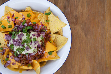 Nachos with chili. Closeup view of nachos with cheddar cheese, avocado cream, red onion pickles and meat sauce in a white bowl.