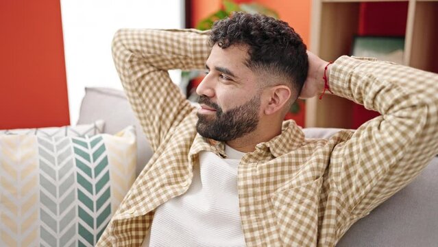 Young hispanic man relaxed with hands on head sitting on sofa at h