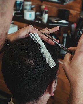 Vertical closeup shot of a male barber working with a comb and scissors to style hair