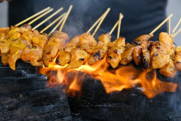 Closeup of grilled chicken satay skewers on fire