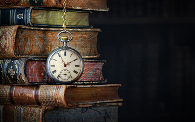 Old clock hanging on a chain on the background of old books.  Сlock as a symbol of time a books...