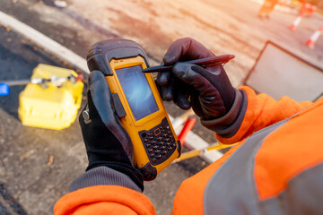 Site engineer operating his touch screen controller instrument during roadworks. Builder using...