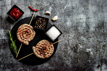 spiral sausages on skewers on a grill on a stone background