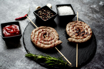 spiral sausages on skewers on a grill on a stone background