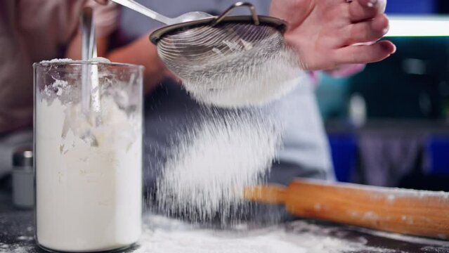 Close-up of a woman sifting flour through a sieve and children helping her. A family is making dough together in the kitchen. High quality 4k footage
