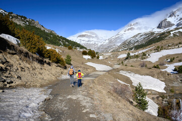 Obraz premium mother and son walking in the snowy mountain next to a river and snowfields. precocious mountain in the pyrenees