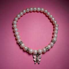 Obraz premium closely made of pink beads with a butterfly pendant a necklace for dogs lies on a pink background. side view . dog accessories gift