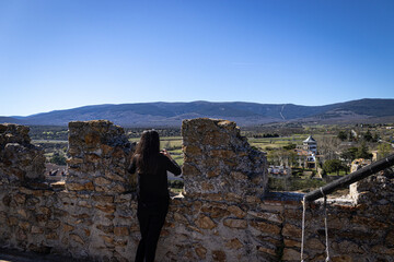 Mujer mirando hacia las montañas de la Sierra Norte de Madrid desde los muros del castillo de Buitrago del Lozoya - obrazy, fototapety, plakaty