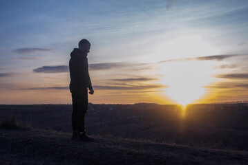 Fototapeta premium A man stands against the background of the sunset. Silhouette of a person. Repentance for sins. Prayer.