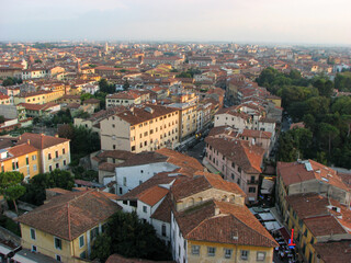 Pisa, Italy - An aerial view from the tower of Pisa's old town, including orange rooftops, in front of a hazy horizon.