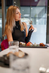 Beautiful young woman with appetizers on dining table holding wineglass in modern restaurant while enjoying vacation at luxurious hotel, luxury vacation concept