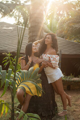 Vertical smiling, relaxed brunette women in summer dress talking and joking near palm tree,...