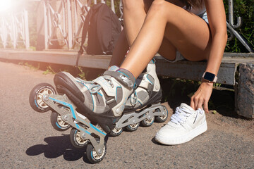 Close up girl putting on inline skates rollers preparing in public park in summer. Teenager leisure...