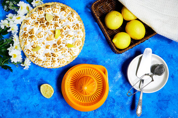 Traditional french lemon Meringue tart with fruits and orange juicer squeezer on blue background