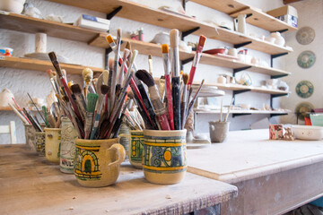 Lots of brushes resting on a table and some pottery behind. Art classes. Instruments and materials...