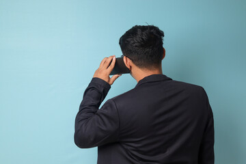 Portrait of young Asian business man in casual suit facing back while talking to phone. Isolated image on blue background