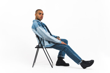 African American male model in full denim outfit sitting on a chair on white background . High quality photo