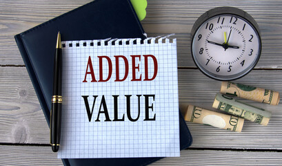 ADDED VALUE - words in a white notebook on the background of an alarm clock and a banknote