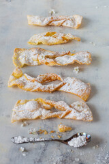 Bow-shaped dry crunchy cookies,  deep-fried pastry ribbons, kind of sugared fritter, a popular dessert from Poland, cakes with powdered sugar on an old rustic white table, high-key photography.