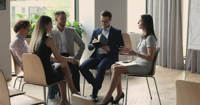 Motivated female business leader sharing ideas with team on office briefing. Group of professionals sitting in circle, brainstorming on project, talking, discussing work tasks strategy