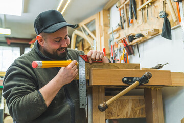 Happy male carpenter marking on wood with big pencil. Variety of tools used in carpentry - bracket...