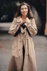 Fototapeta premium Elegant young girl in a beige raincoat posing outdoors