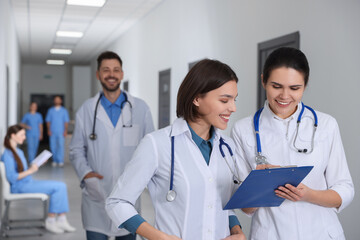 Smart medical students with clipboard in college hallway, space for text