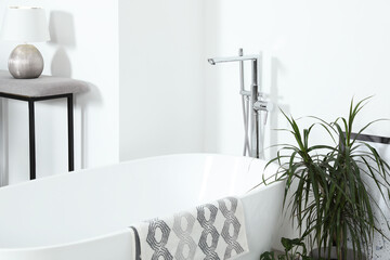 Stylish white tub and green houseplants in bathroom. Interior design