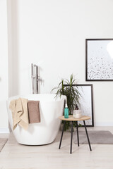 Stylish white tub and wooden table with toiletries in bathroom. Interior design