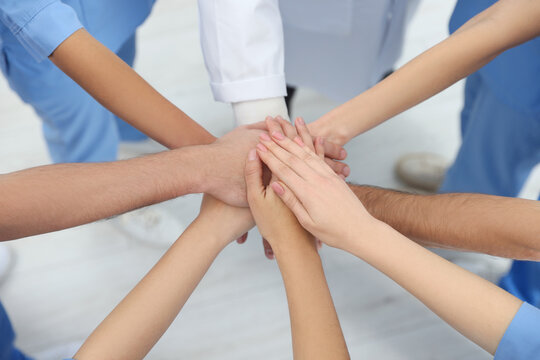 Doctor and interns stacking hands together indoors, closeup