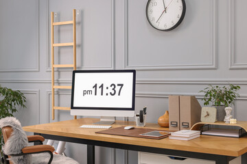 Stylish workplace with computer, houseplants and stationery on wooden desk near grey wall at home