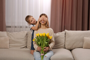 Little daughter congratulating mom with bouquet of yellow tulips at home. Happy Mother's Day