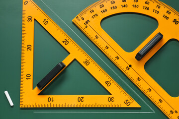 Protractor, triangle and chalk on green chalkboard, flat lay