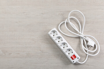 Power strip with extension cord on white wooden floor, top view. Space for text