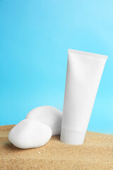 Tube of cream and stones on sand against light blue background. Cosmetic product