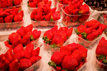 Strawberries with green weed in plastic containers at marketplace