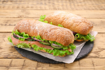 Delicious sandwiches with fresh vegetables and salmon on wooden table, closeup