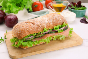 Delicious sandwich with fresh vegetables and salmon on white table, closeup