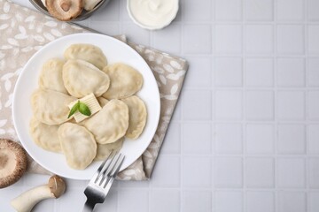 Delicious dumplings (varenyky) with mushrooms and butter served on white tiled table, flat lay. Space for text