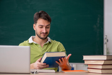 Young male student sitting in front of green board