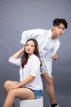 elegant men and women posing standing in front of the camera while the ladder holding the hair and hotpen in the indoor. fashion promotion couple shirt photo session in gray background studio