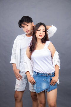 elegant men and women posing standing in front of the camera while the ladder holding the hair and hotpen in the indoor. fashion promotion couple shirt photo session in gray background studio