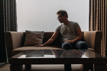 Fototapeta premium Lonely asian man sits on the sofa thinking of his lover.