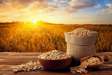 oat flakes in bowl and grains in sack on table with ripe cereal field on sunset as background