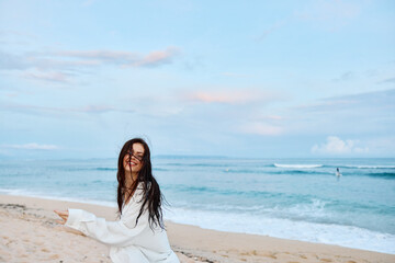 Fototapeta na wymiar Brunette woman with long hair in a white shirt and denim shorts smile and happiness running on the beach and having fun smile with teeth in front of the ocean, vacation summer trip