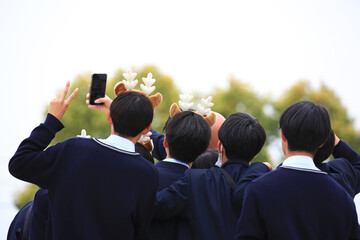 Young male Japanese students with deer antlers taking a group selfie outside Todaji Temple in Nara, Japan.