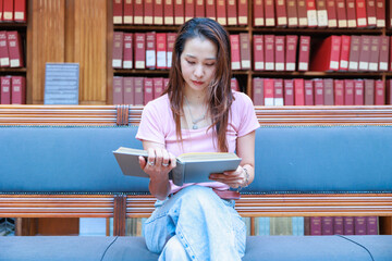 図書館の長椅子に座って本を読む大学生