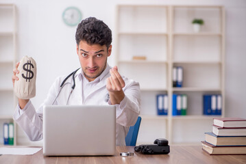 Young male doctor holding moneybag in the clinic